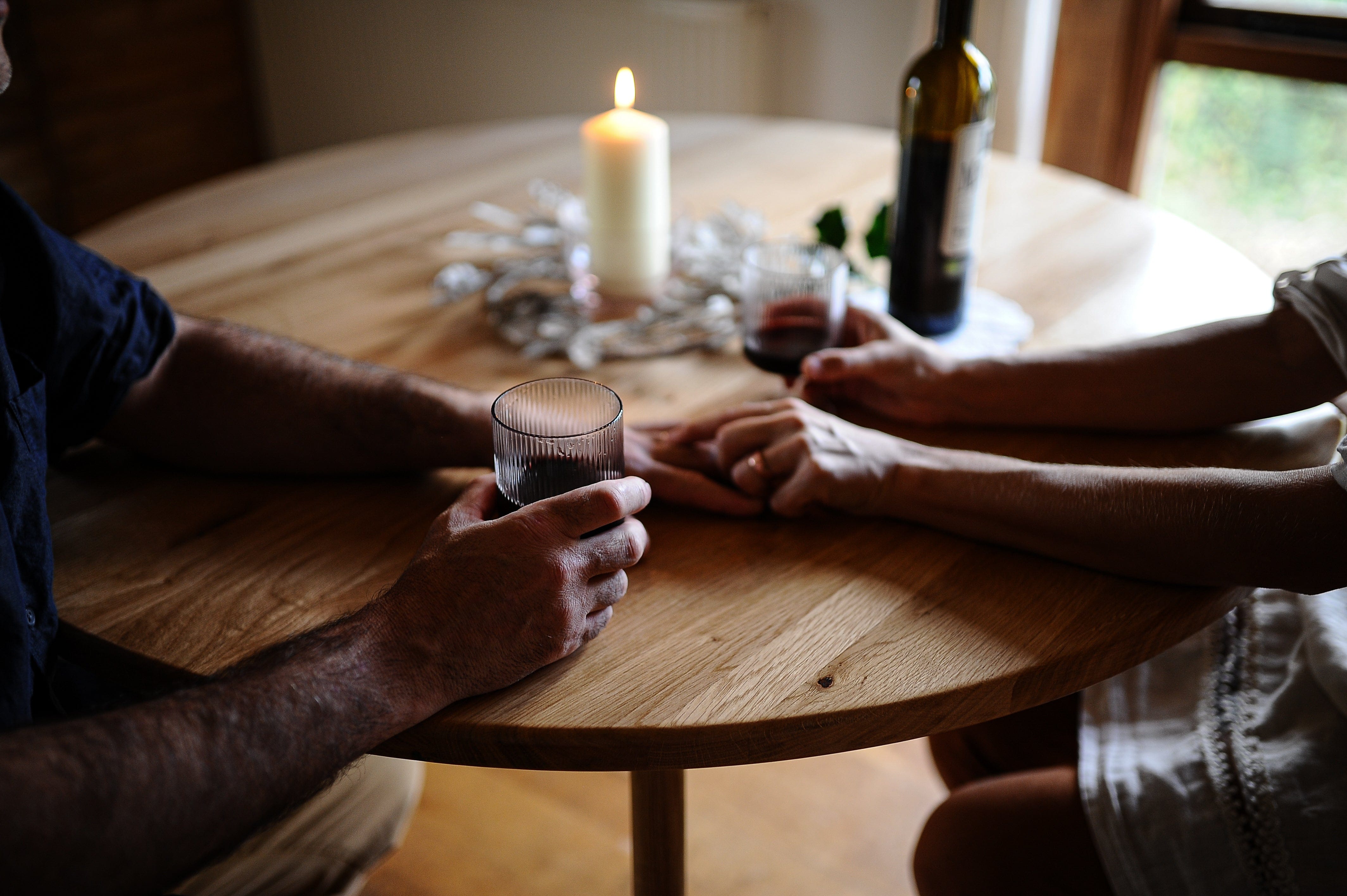 solid oak round dining table in natural finish from the oakwell collection in modern dining room with couple holding hands and drinking red wine.