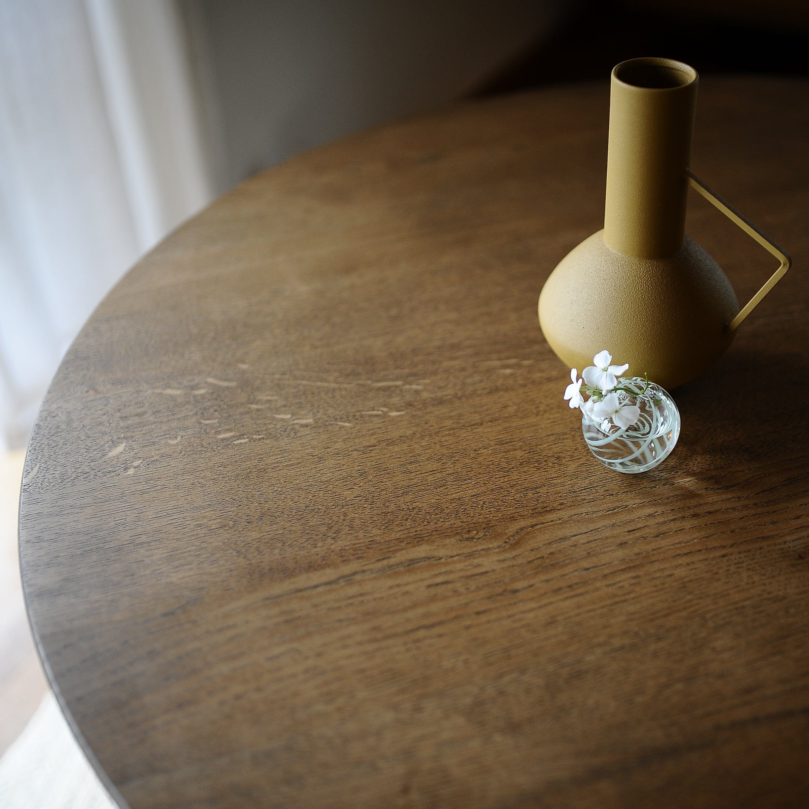 Sophia round dining table in solid prime oak with a smoked finish, with decorative jug and vase with flower