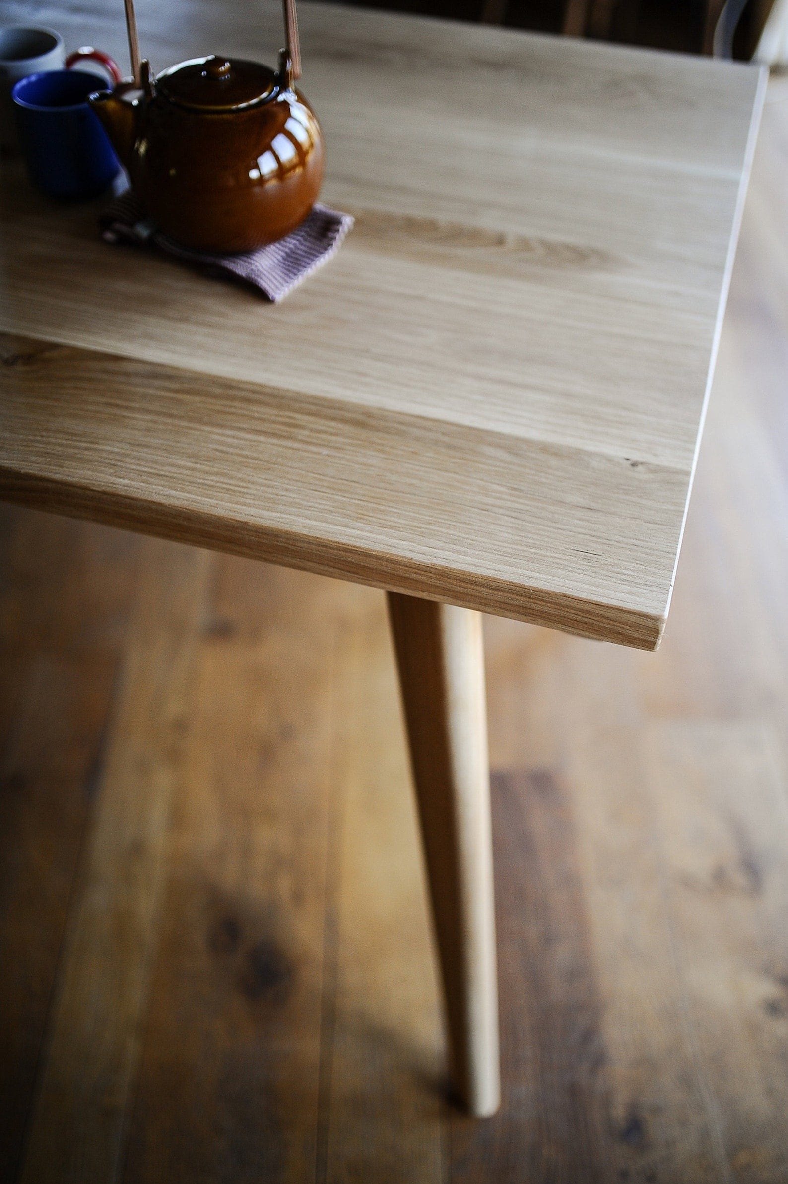 rectangular solid oak dining table with tapered oak legs and round teapot and mugs. Dining set from the oakwell collection