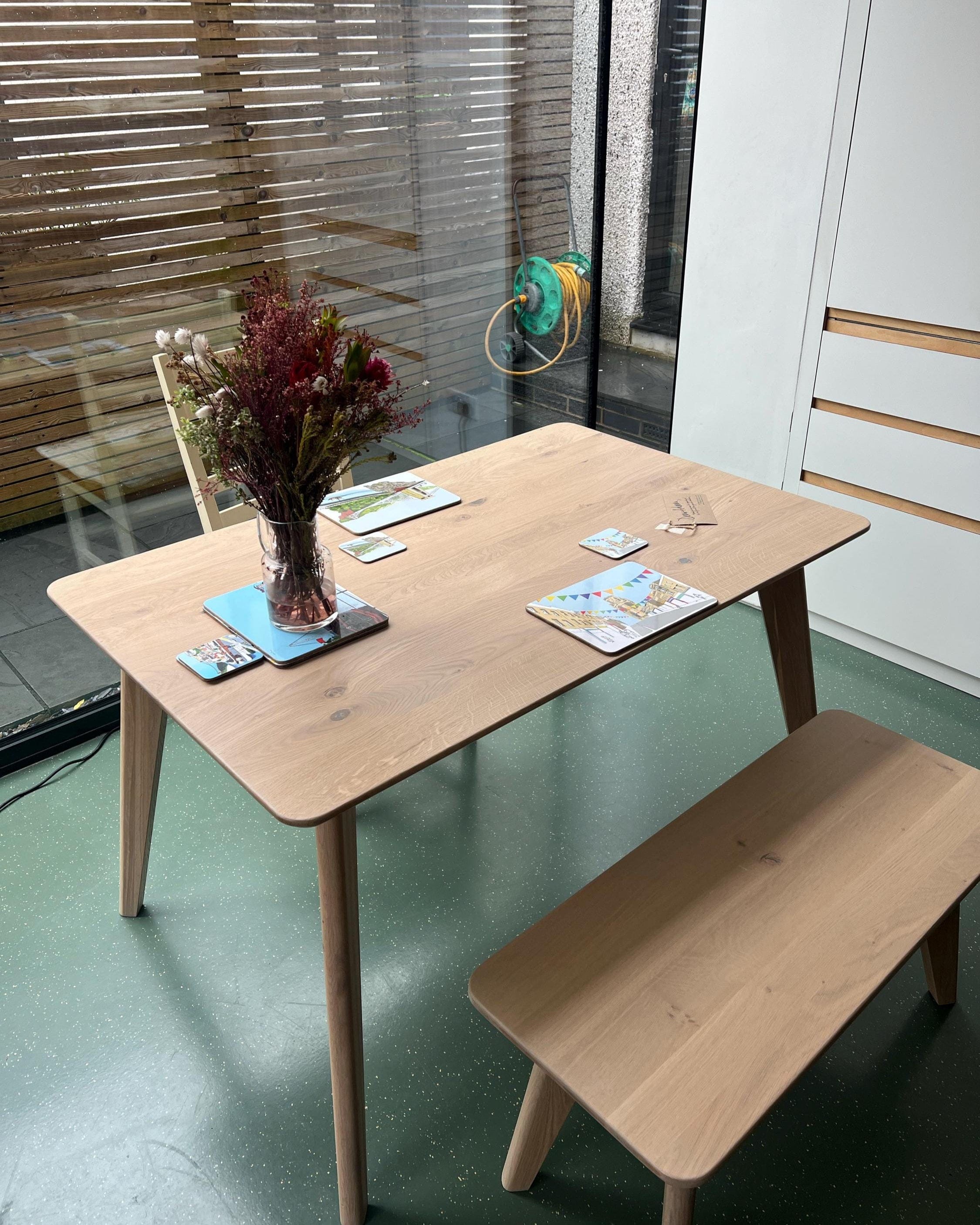 Wooden dining table with bench in a room with green floor and large window.