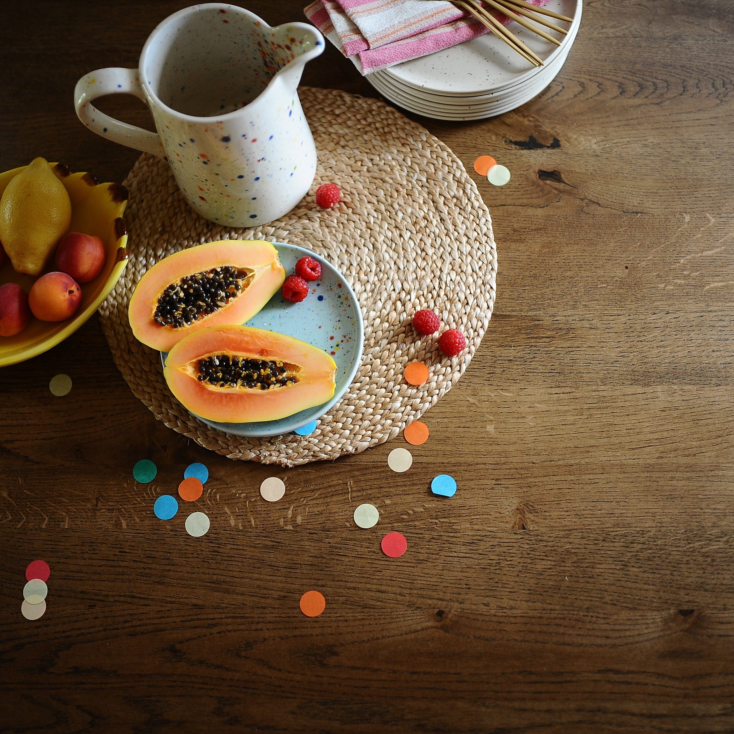 Papaya slices on a plate with a pitcher and fruit bowl on a wooden table.