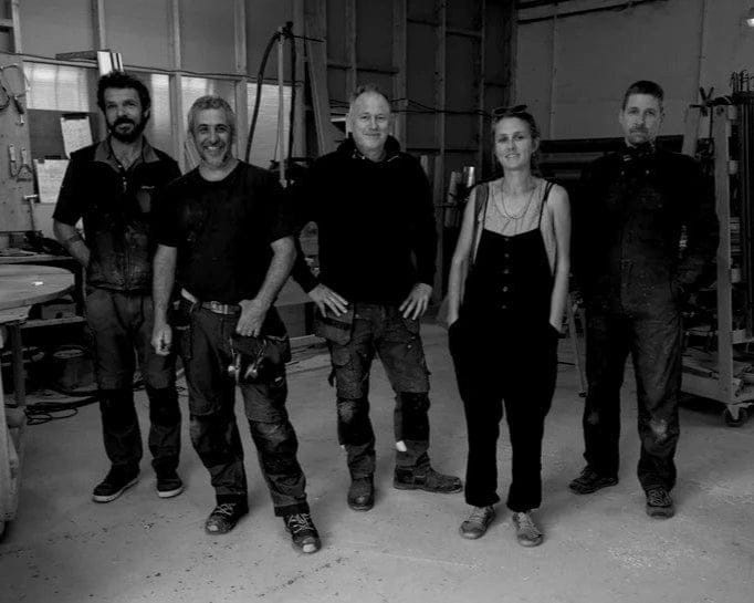Group of five people standing together in a workshop or industrial setting.