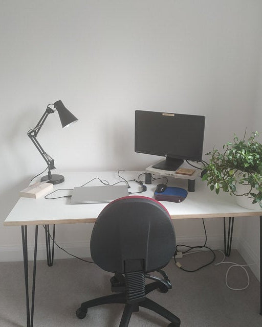 Home office setup with a desk, chair, computer monitor, lamp, and plant.