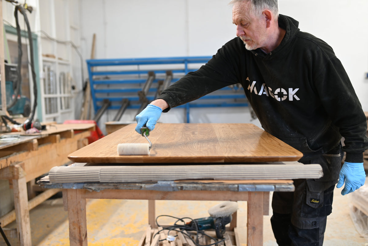 Craftsman applying hard wax oil to a handcrafted solid oak table top in a woodworking workshop during the recoating process