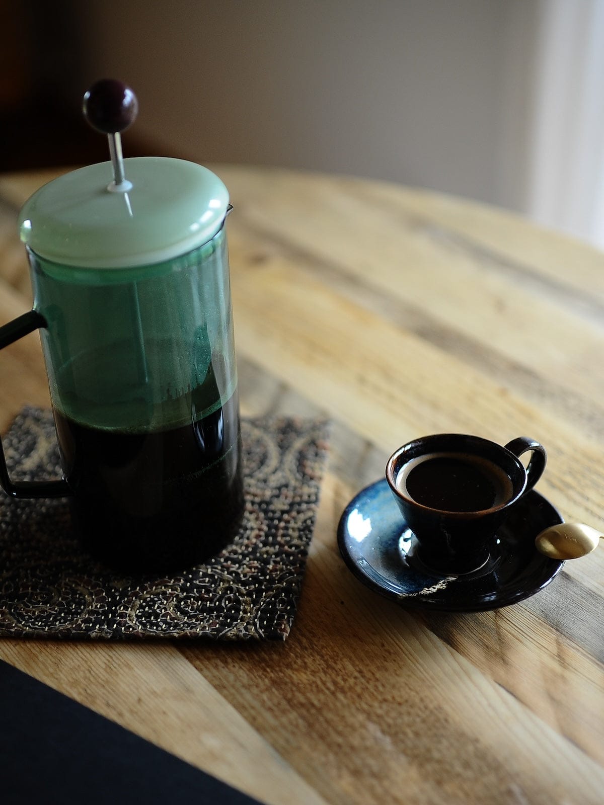 French press with coffee and a small cup on a solid reclaimed wood table