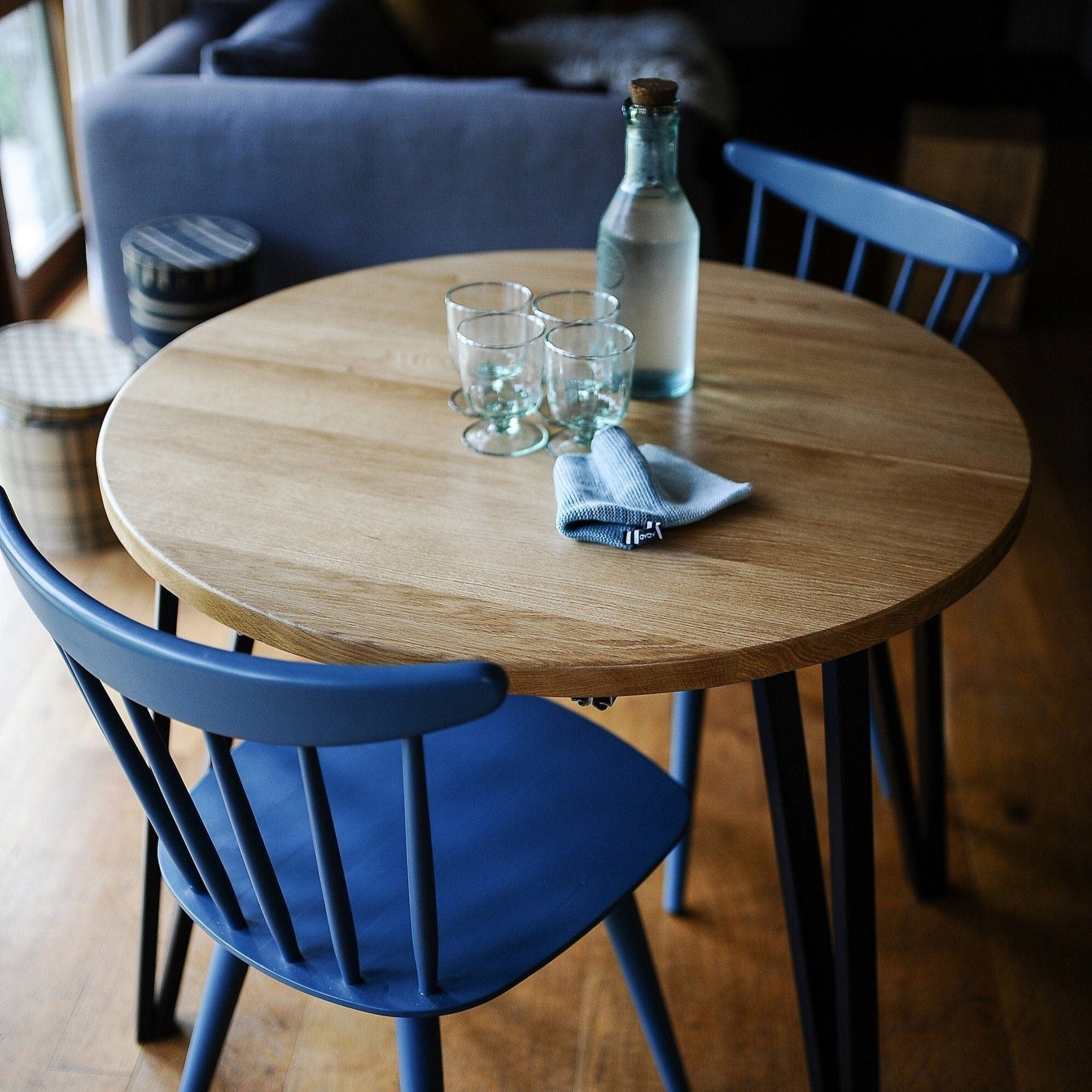 Round wooden table with blue chairs and glasses on a wooden floor.