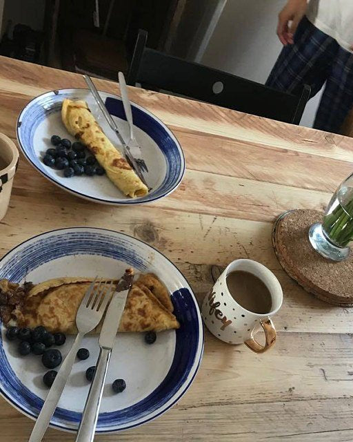 Two plates of food with blueberries, a mug, and a vase on a wooden table.